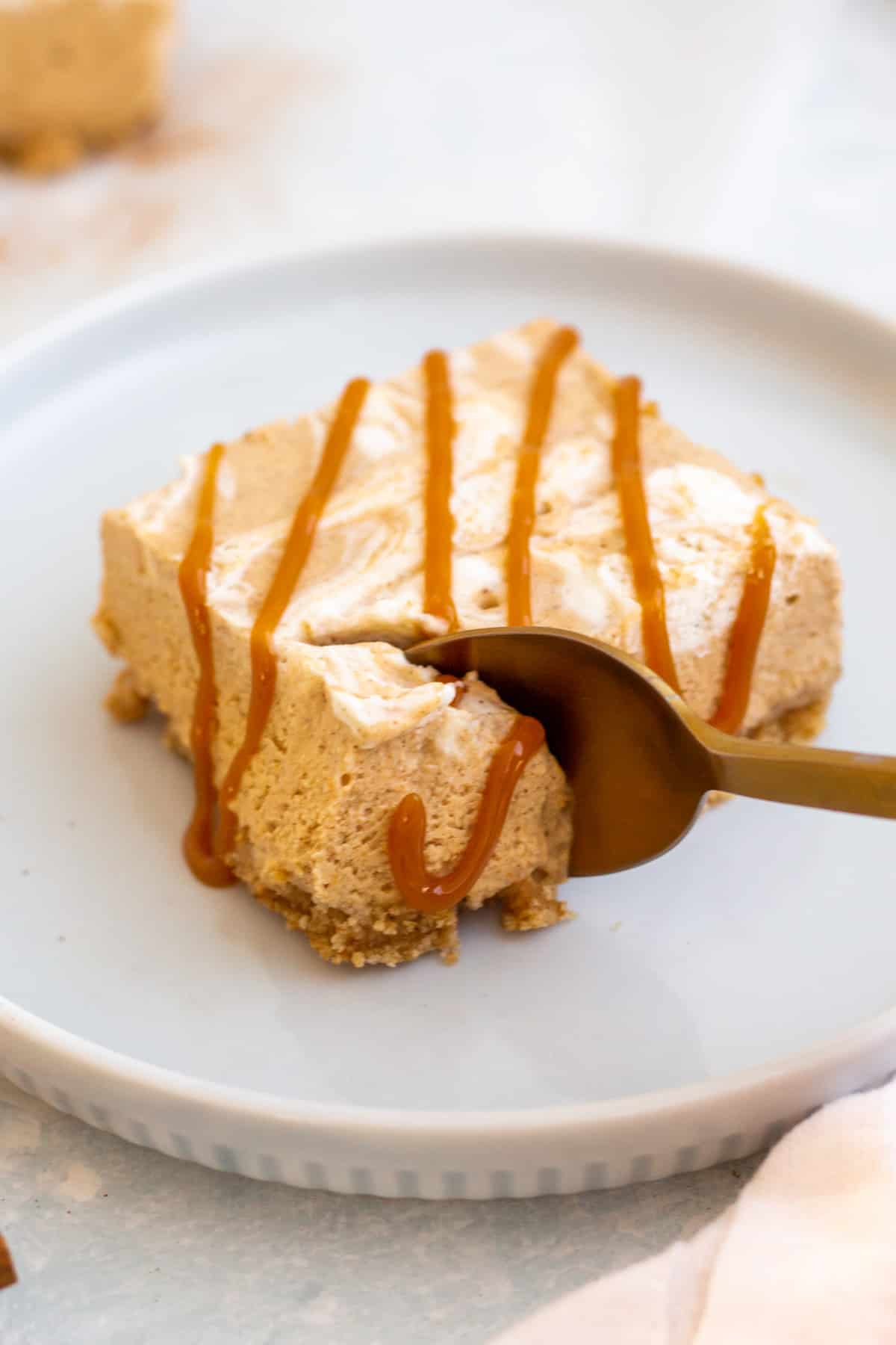 spoon cutting into pumpkin cheesecake bar with caramel drizzle