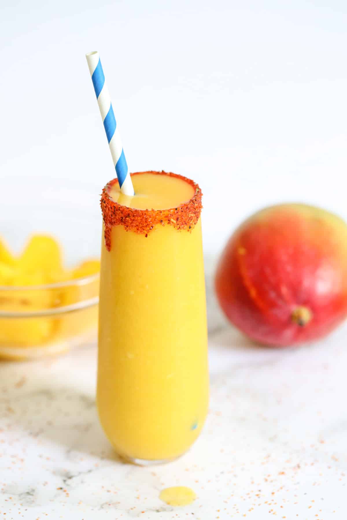 mangonada smoothie in a glass with a blue straw and a mango fruit