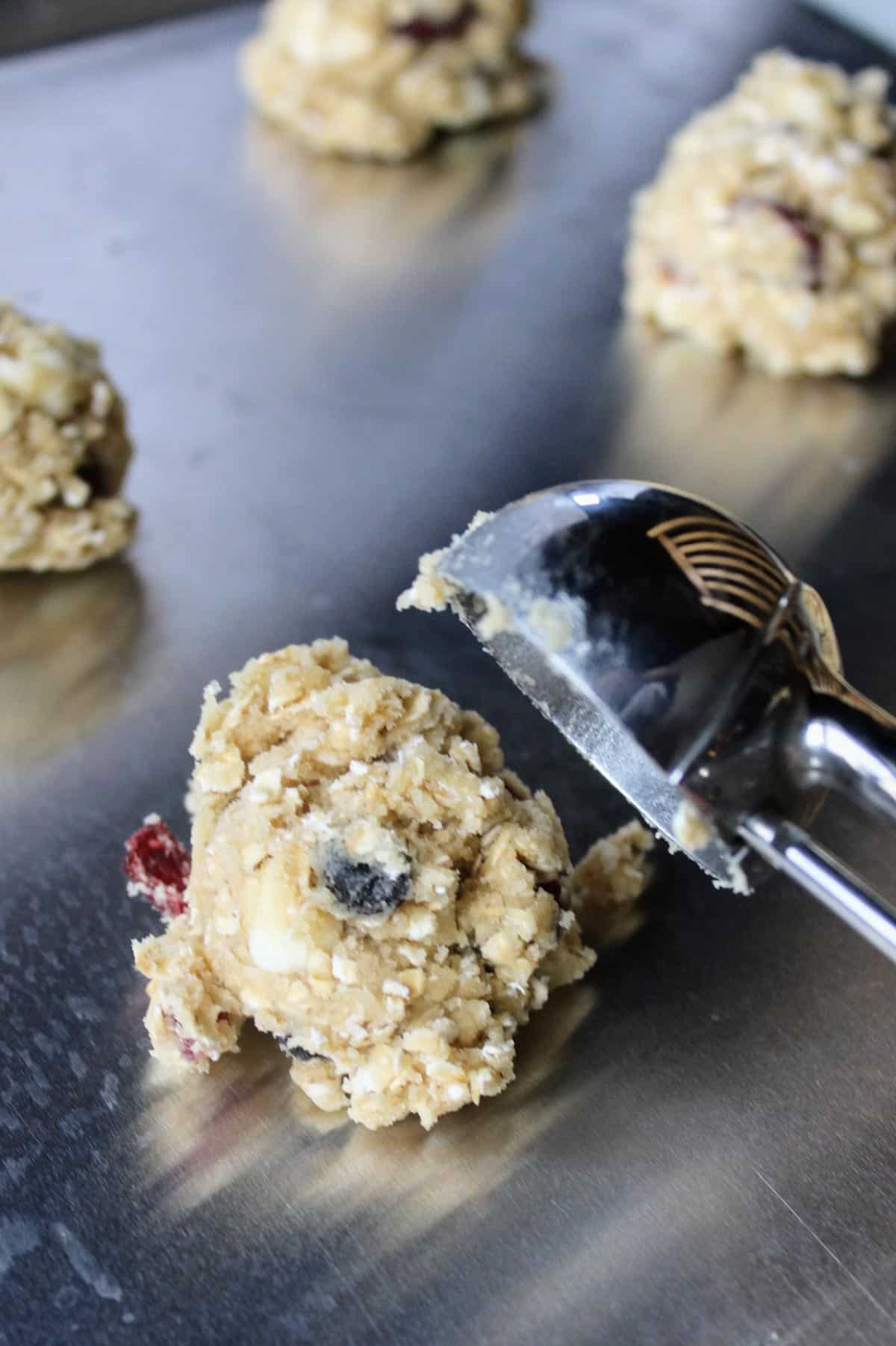 adding cookies to a baking sheet using an ice cream scoop