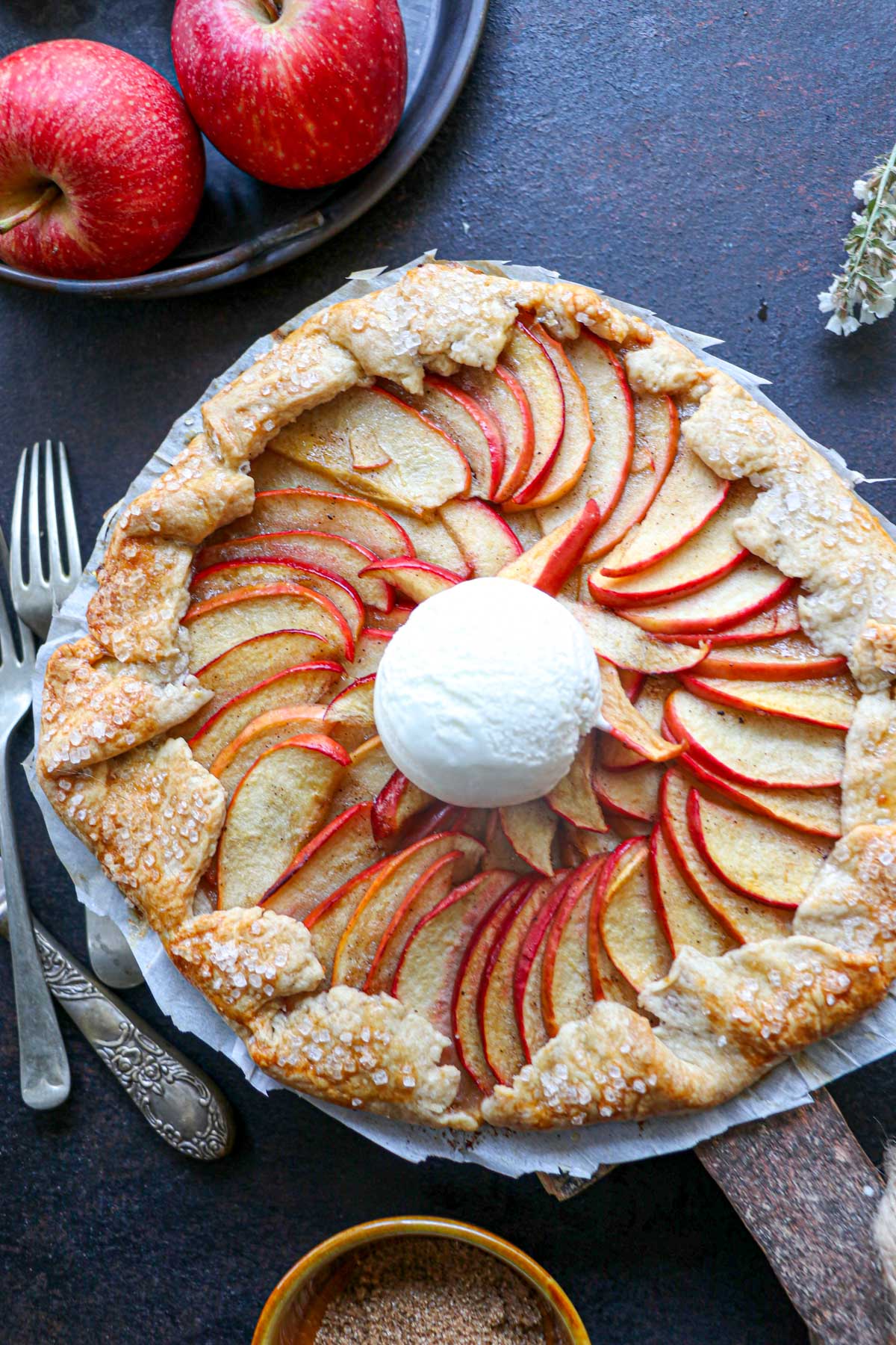 apple galette with a black background and ice cream on top with whole red apples also on the table