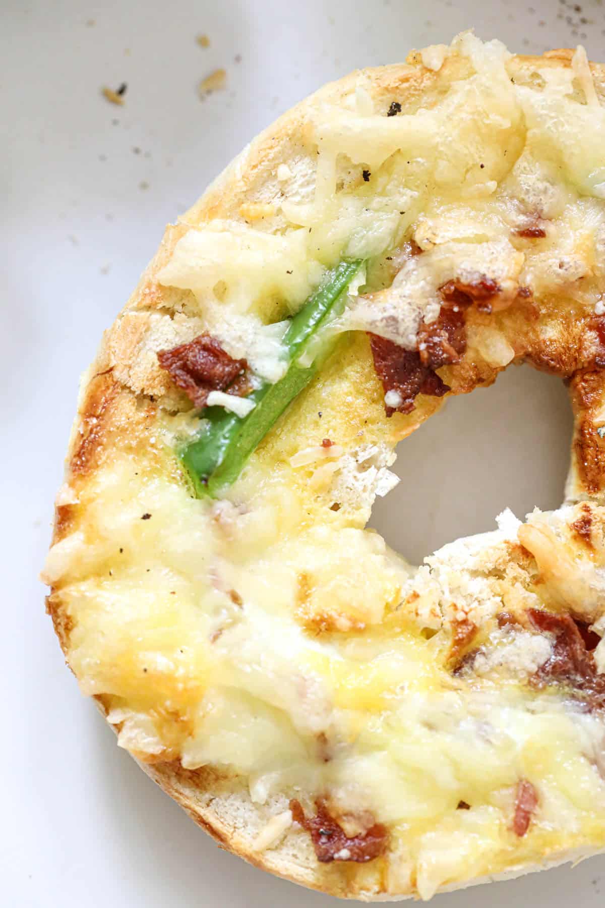 close up of a bagel with green pepper, bacon, and cheese