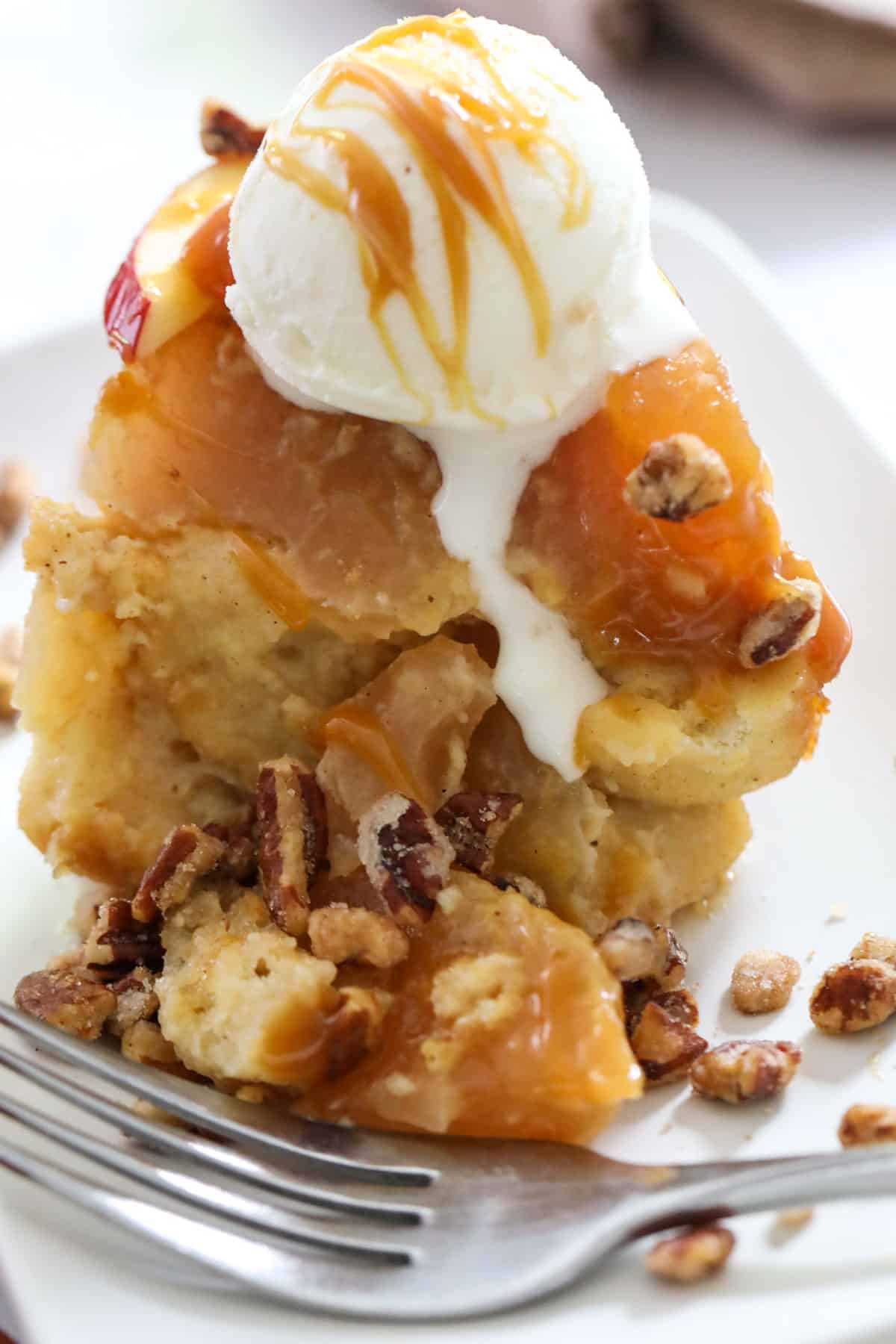 apple pie bread pudding with a fork and candied nuts and ice cream on top