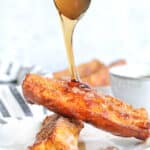 a spoon adding syrup to french toast sticks stacked on a plate