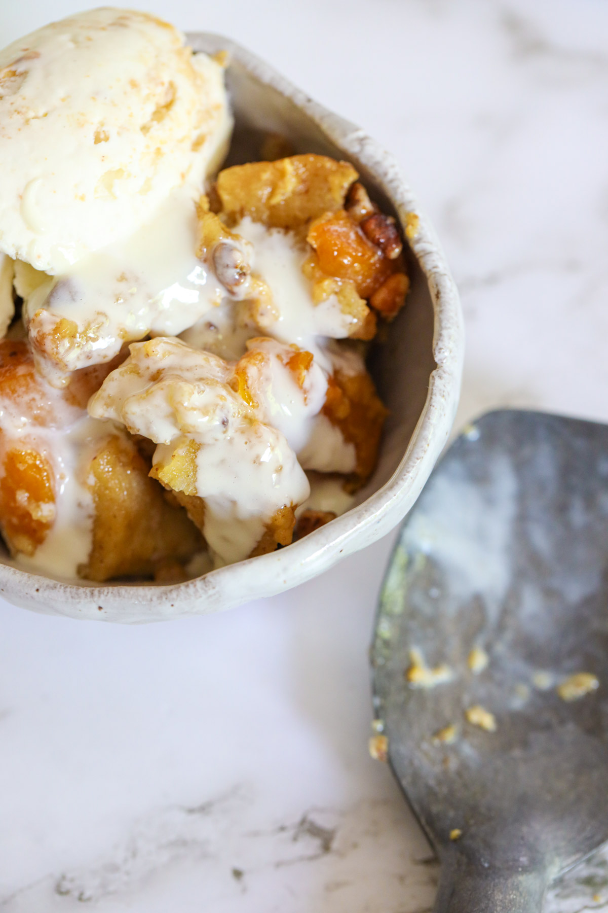 vanilla ice cream and peach bread pudding in a bowl with an ice cream 