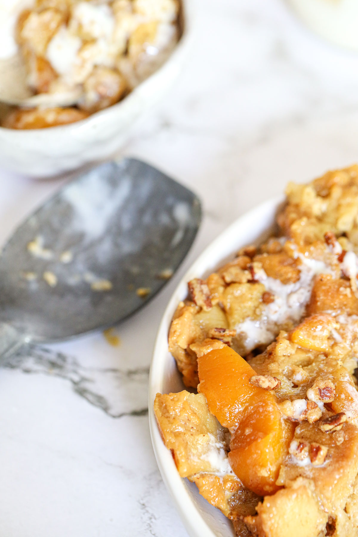 peach bread pudding in a bowl with an ice cream scoop near