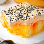 orange striped poke cake with a fork and spoon and black sprinkles