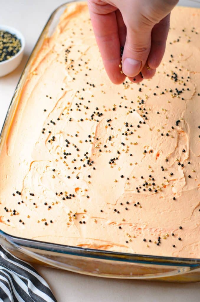 topping the light orange cake with black and gold sprinkles