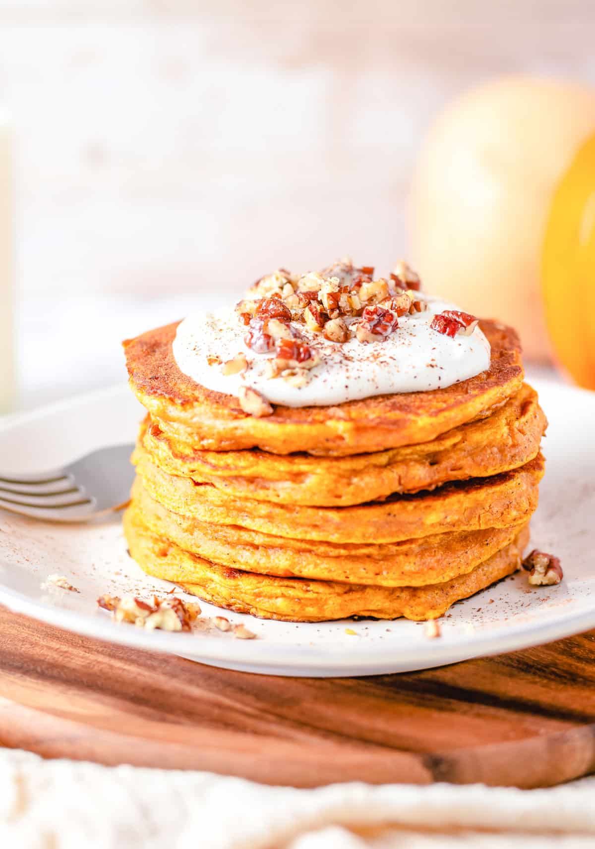 stack of pumpkin pancakes with cream frosting on top and candied nuts