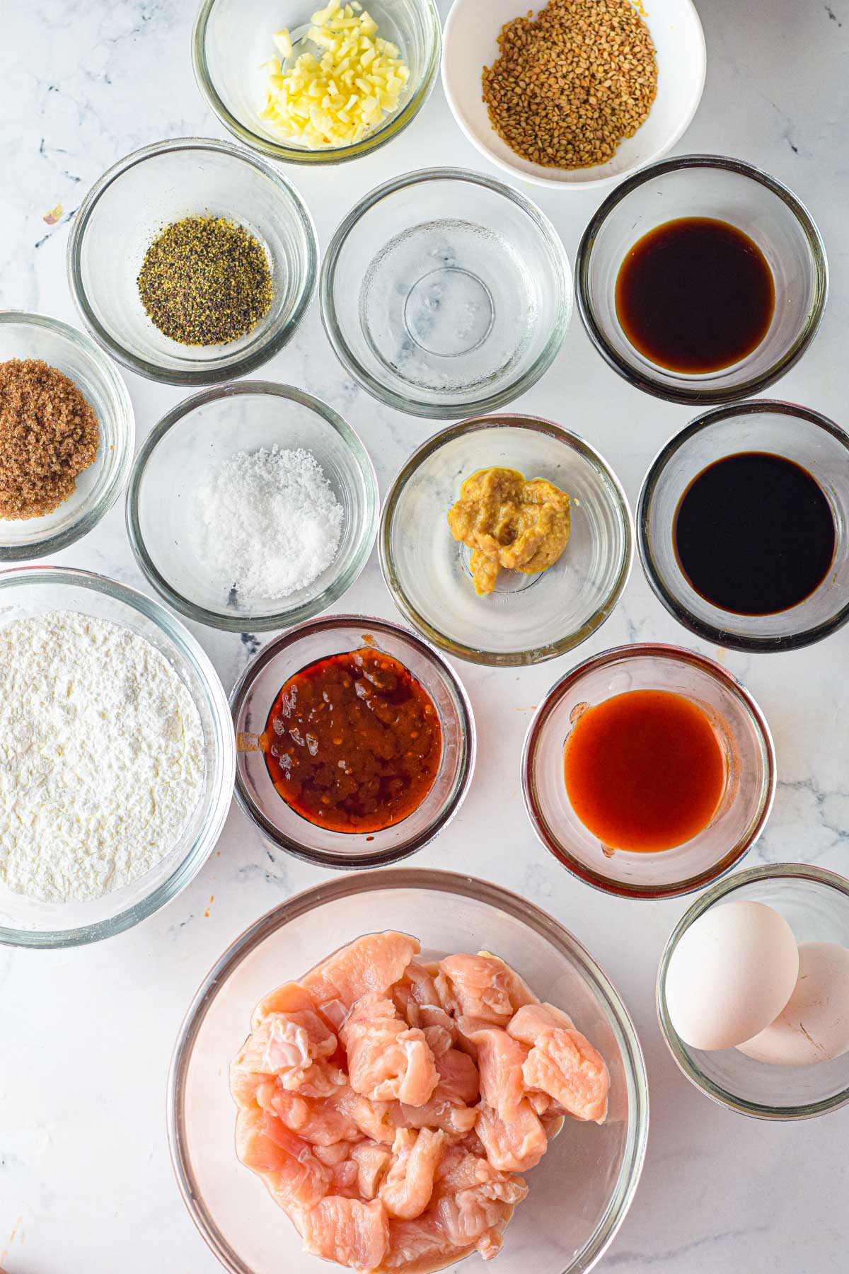ingredients for sesame chicken in clear bowls on a white table