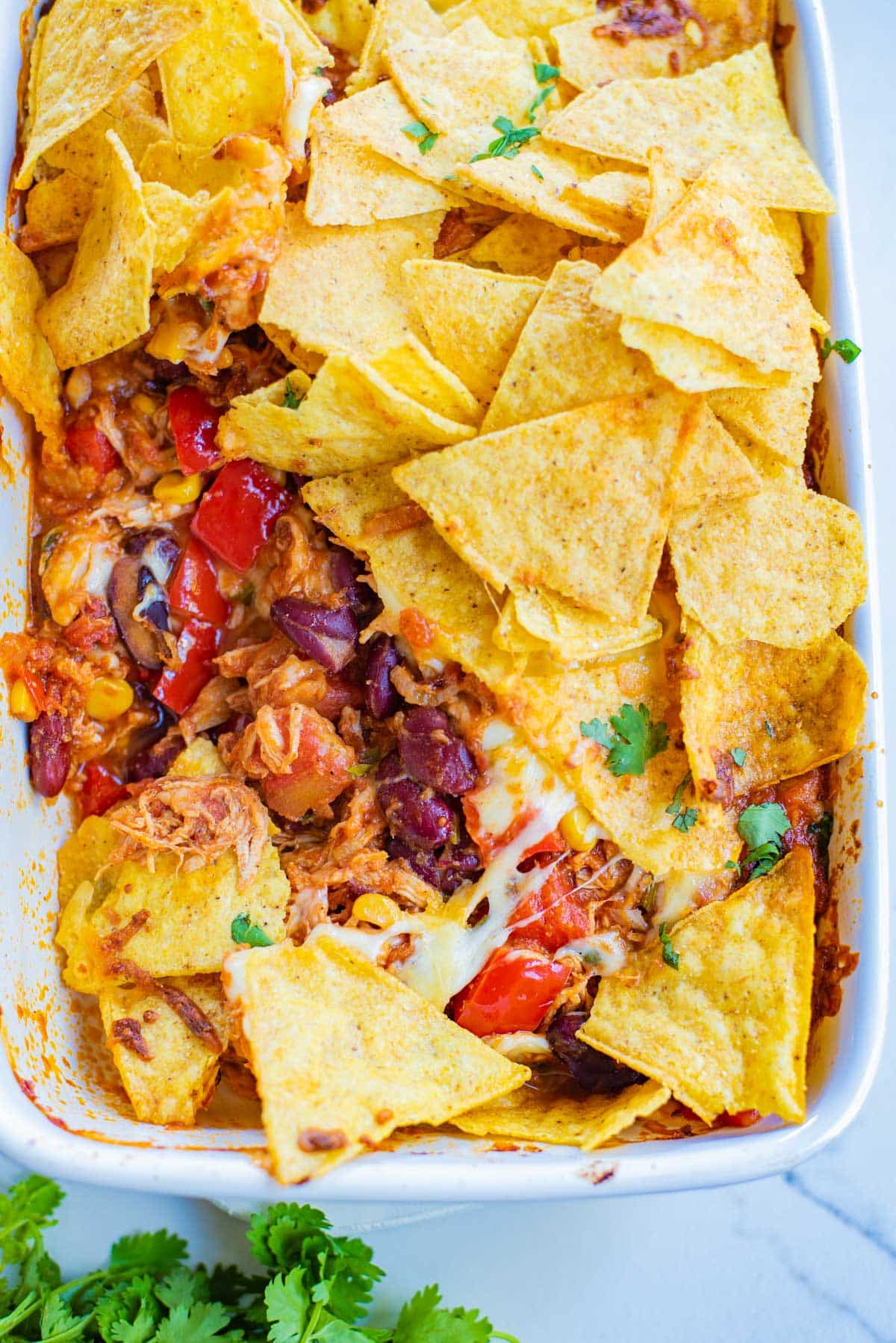 baking dish full of Doritos, chicken, beans, tomatoes, and cilantro on the side