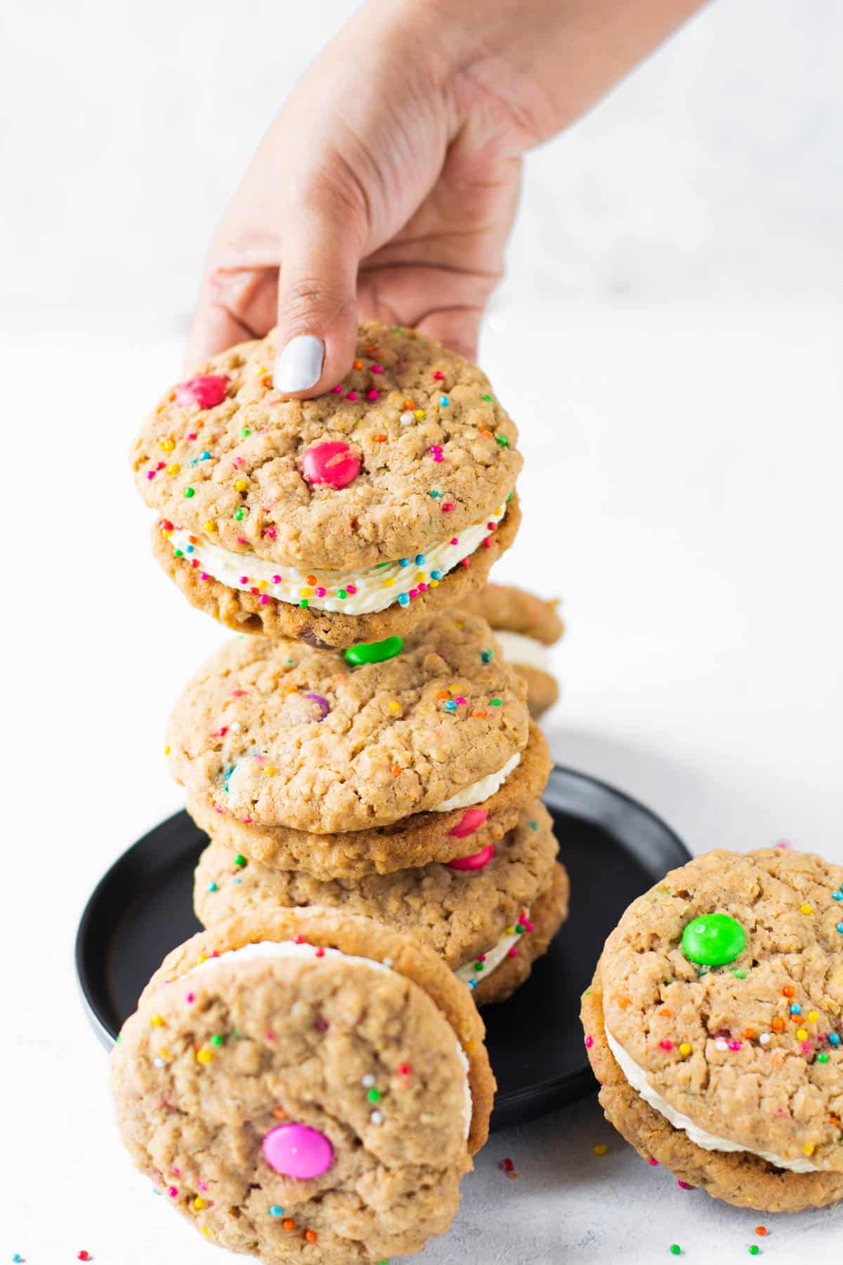 hand grabbing a thick oatmeal whoopie pie monster cookie full of sprinkles and m&m's