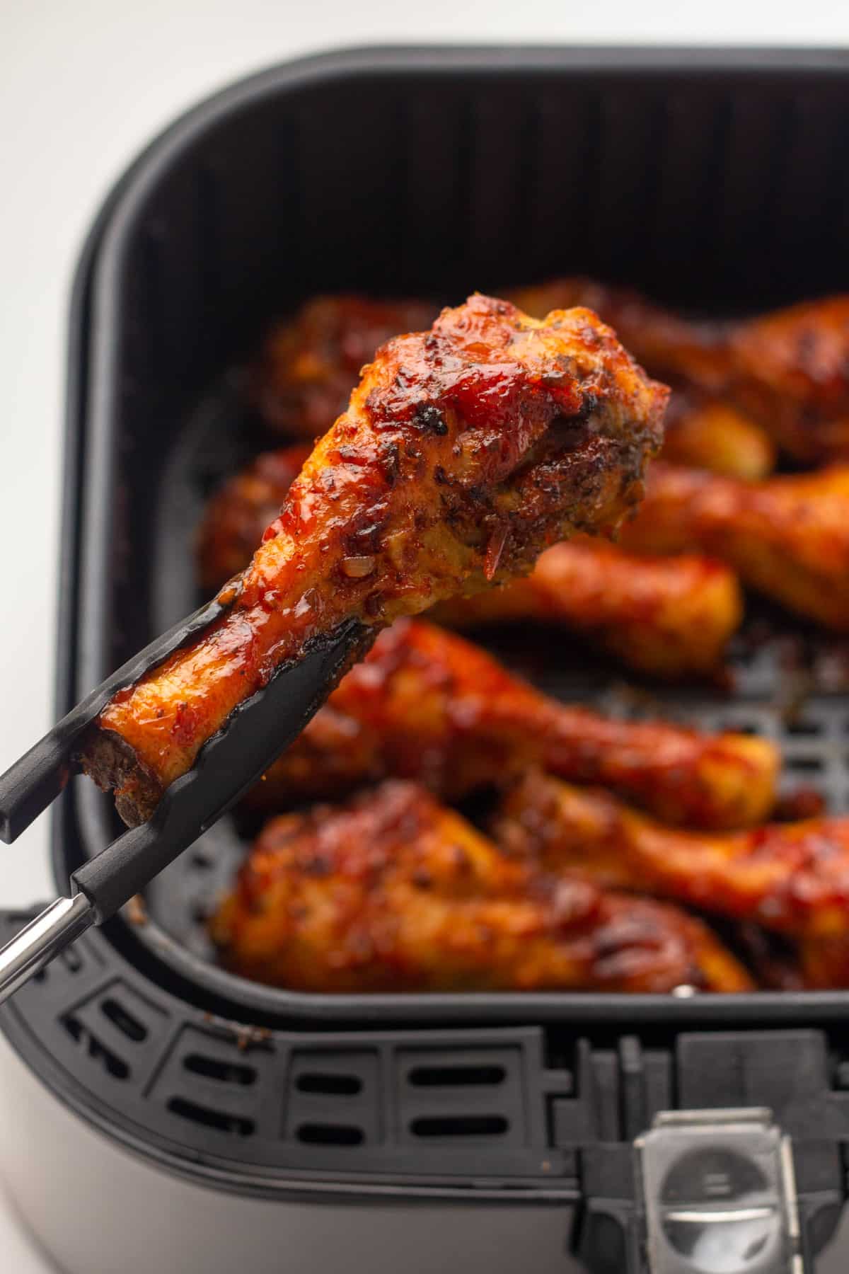 tongs lifting a bbq chicken leg from the air fryer basket