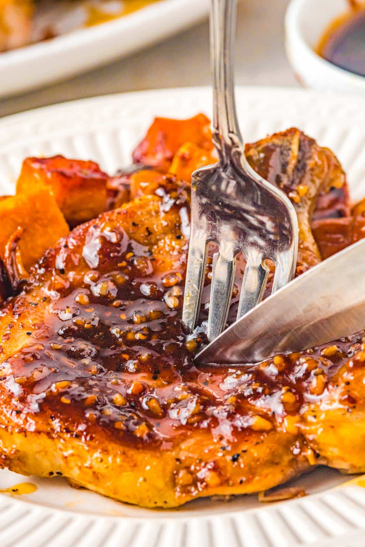 cutting into a juicy glazed pork chop with a knife and fork