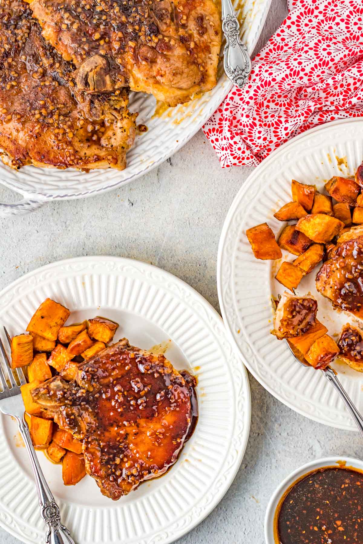 plates full of sweet potatoes and pork chops with bourbon glaze next to a red and white napkin