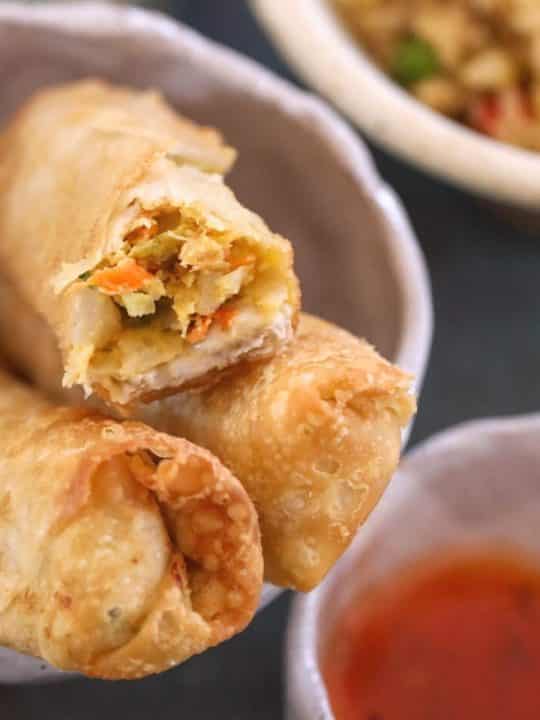 three egg rolls with dipping sauce with a bite taken from one