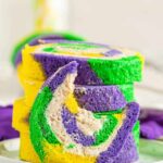 swirled Mardi Gras cake roll with yellow, green and purple and cinnamon cream cheese frosting inside