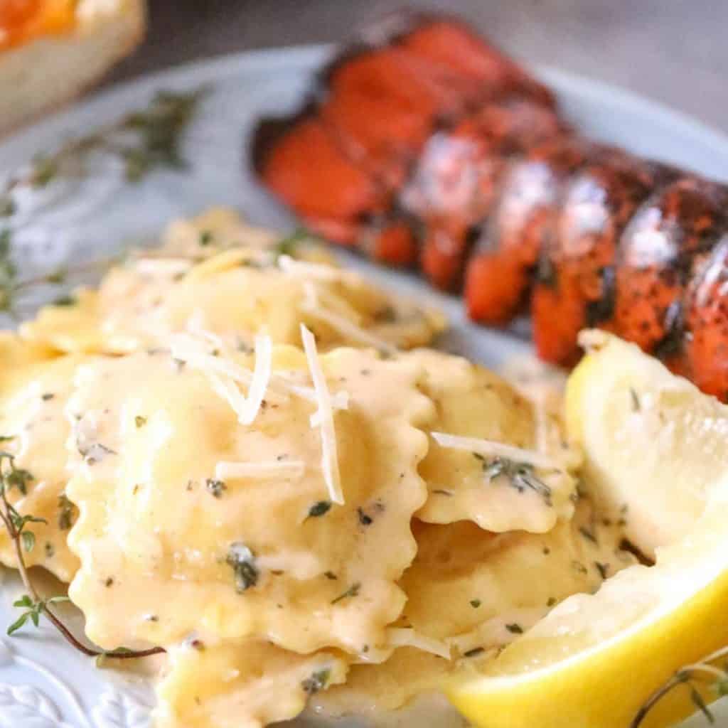 lobster ravioli sauce next to a buttery lobster tail and lemon wedges