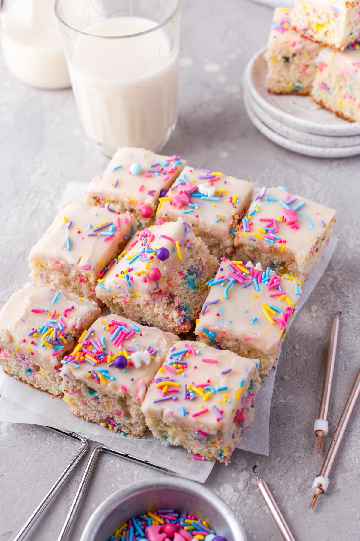 funfetti sprinkled sheet cake sliced into 9 identical pieced with a tall glass of milk