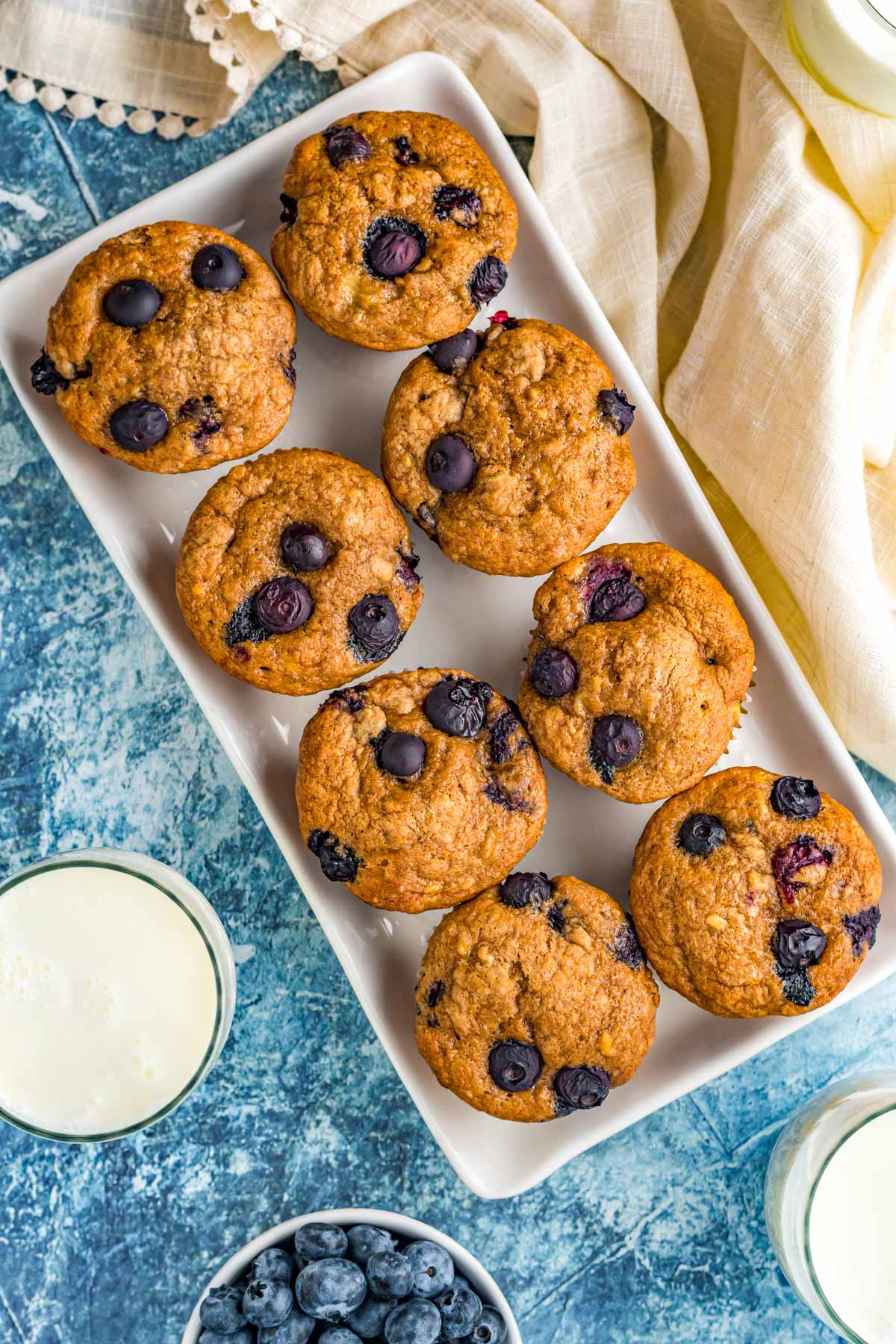 pan with 8 blueberry banana muffins and a cold glass of milk next to fresh blueberries