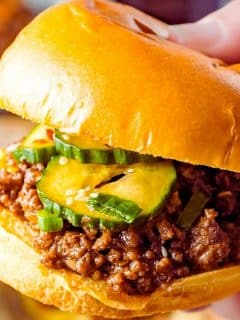 a hand holding a thick and juicy sloppy Joe sandwich with a golden bun
