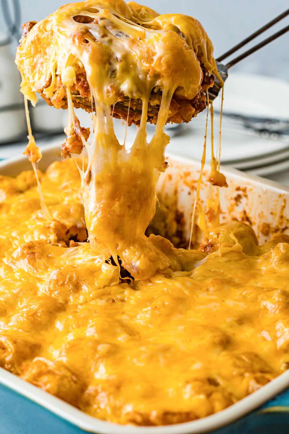 spatula pulling a serving of sloppy joe tater tots casserole from a baking dish with cheese pulling from the edge