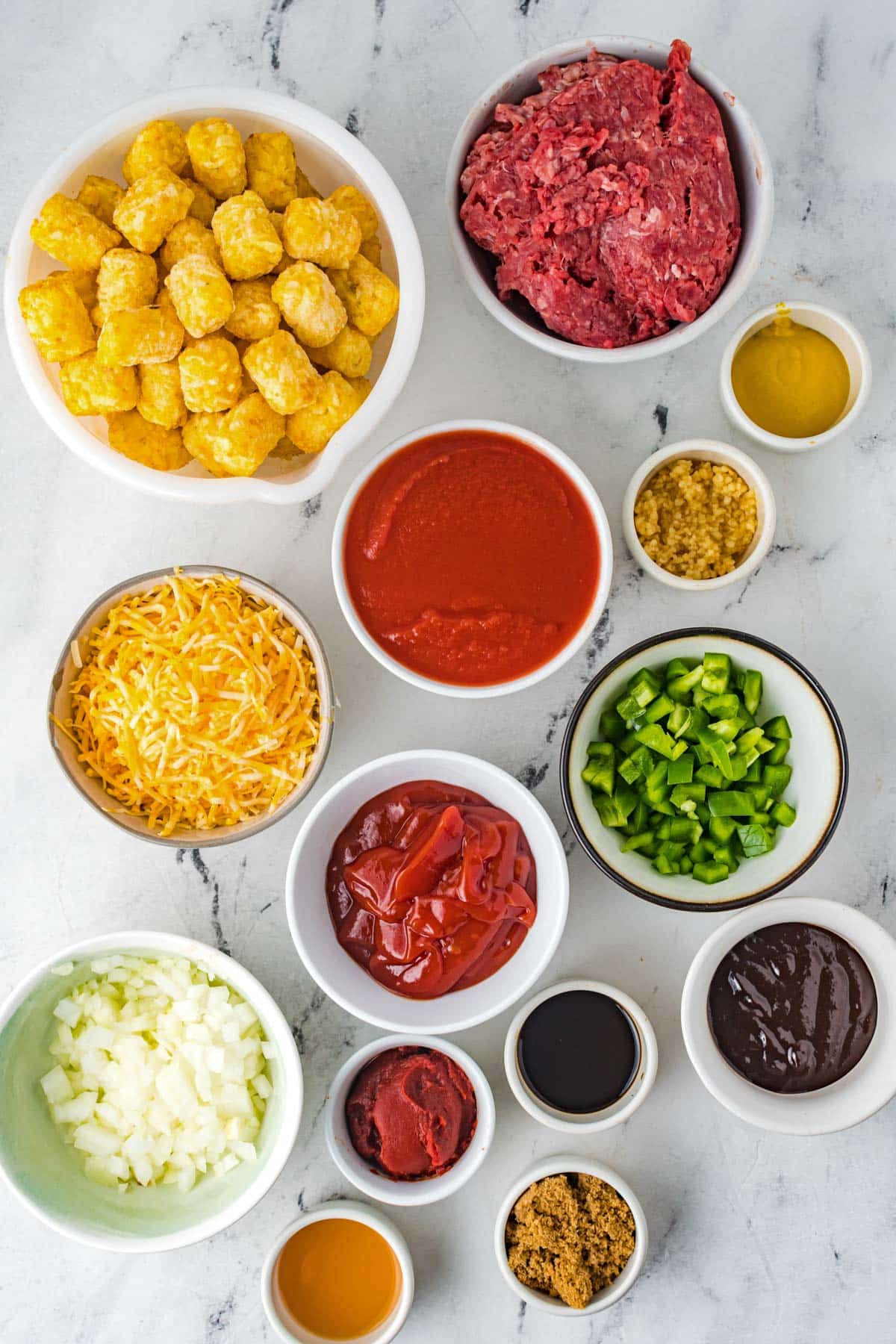 ingredients for sloppy joe tater tot casserole, including onion, cheese, green bell pepper, ketchup, ground beef and brown sugar