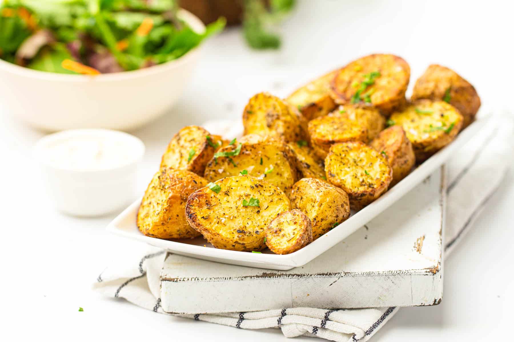 roasted potatoes on a large platter next to a salad and dipping sauce
