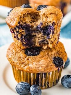 blueberry banana muffins stacked on top of each other with fresh blueberries all around the plate