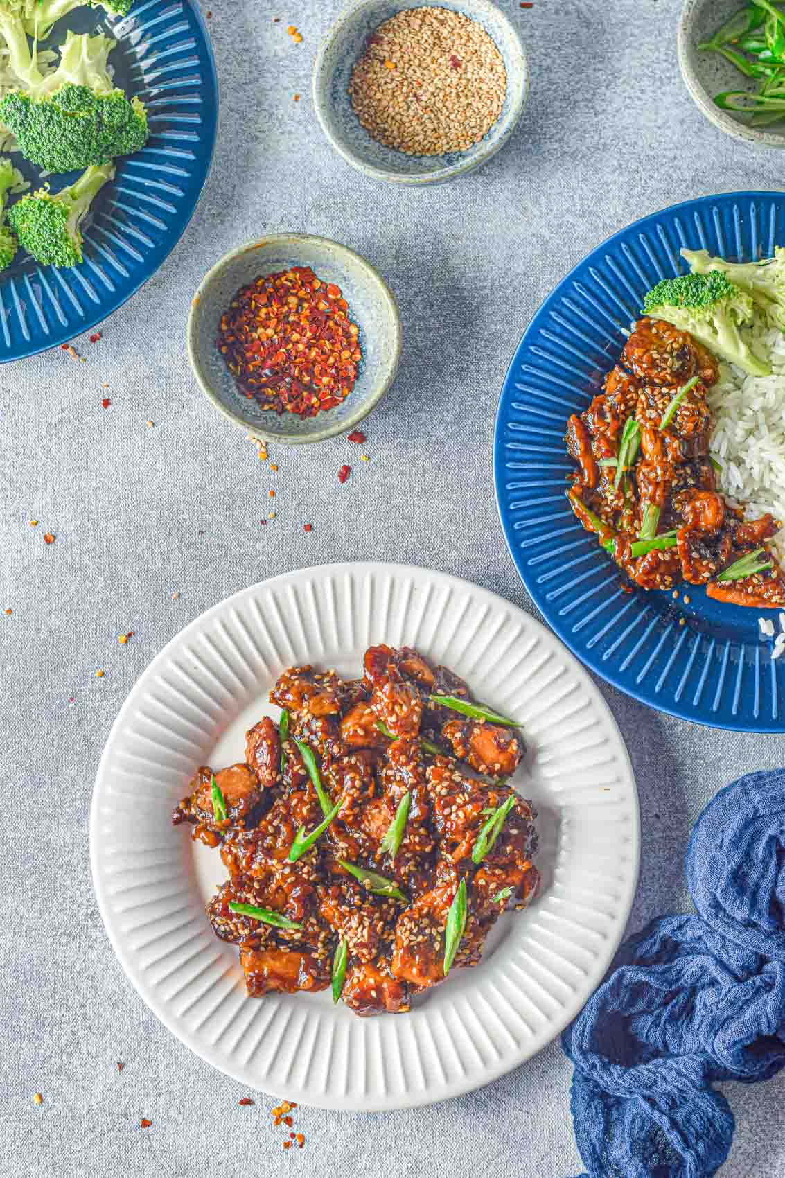 three plates of chicken sesame teriyaki and broccoli on a white and blue plates next to a blue linen