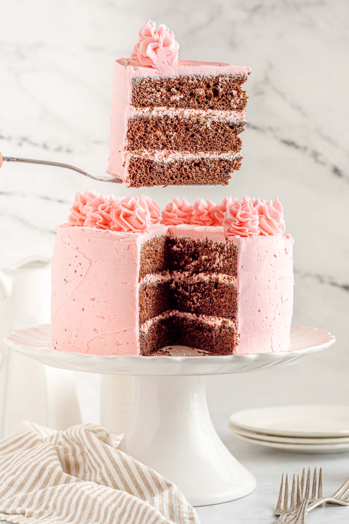 lifting a piece of Kahlua cake from the whole cake, revealing triple layer chocolate and strawberry frosting