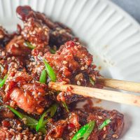 wooden chopsticks holding a piece of teriyaki chicken with green onion as garnish