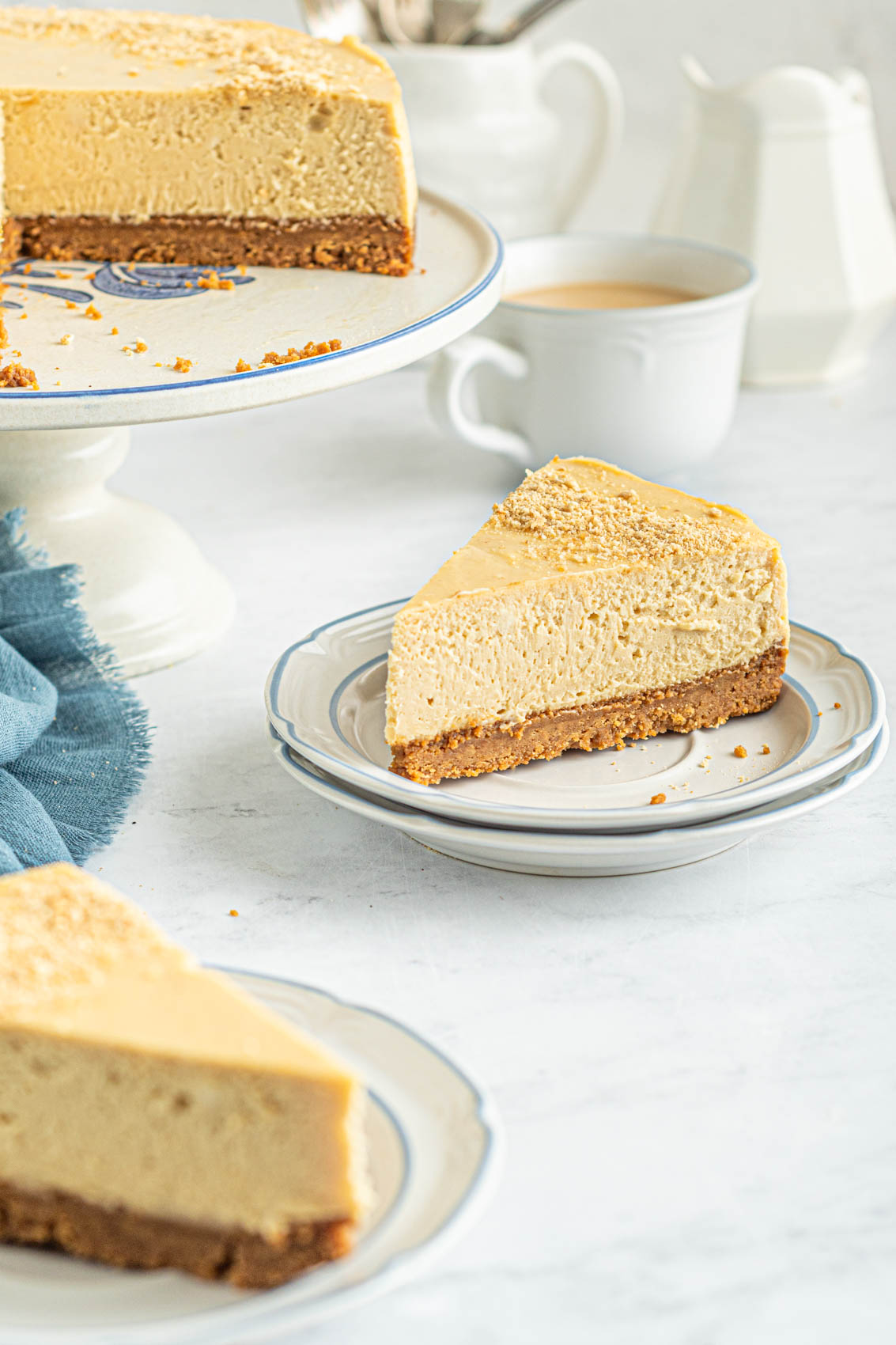 a slice of peanut butter cheesecake next to a blue napkin and a cup of coffee