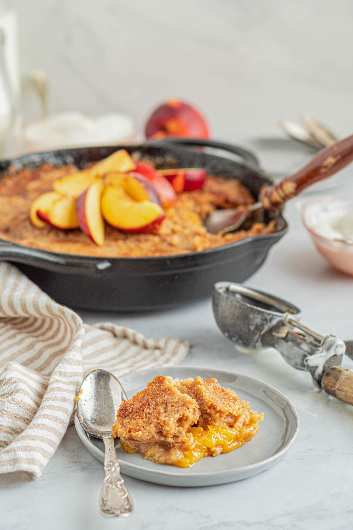 peach cobbler in a cast iron skillet with a spoon and old fashioned spoon