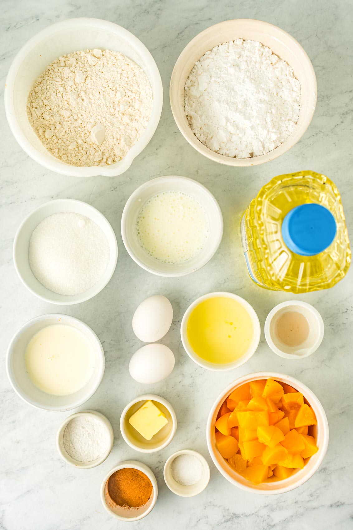 ingredients for peach fritters, including flour, canola oil, canned peaches, vanilla, eggs, milk, cinnamon, sugar and butter
