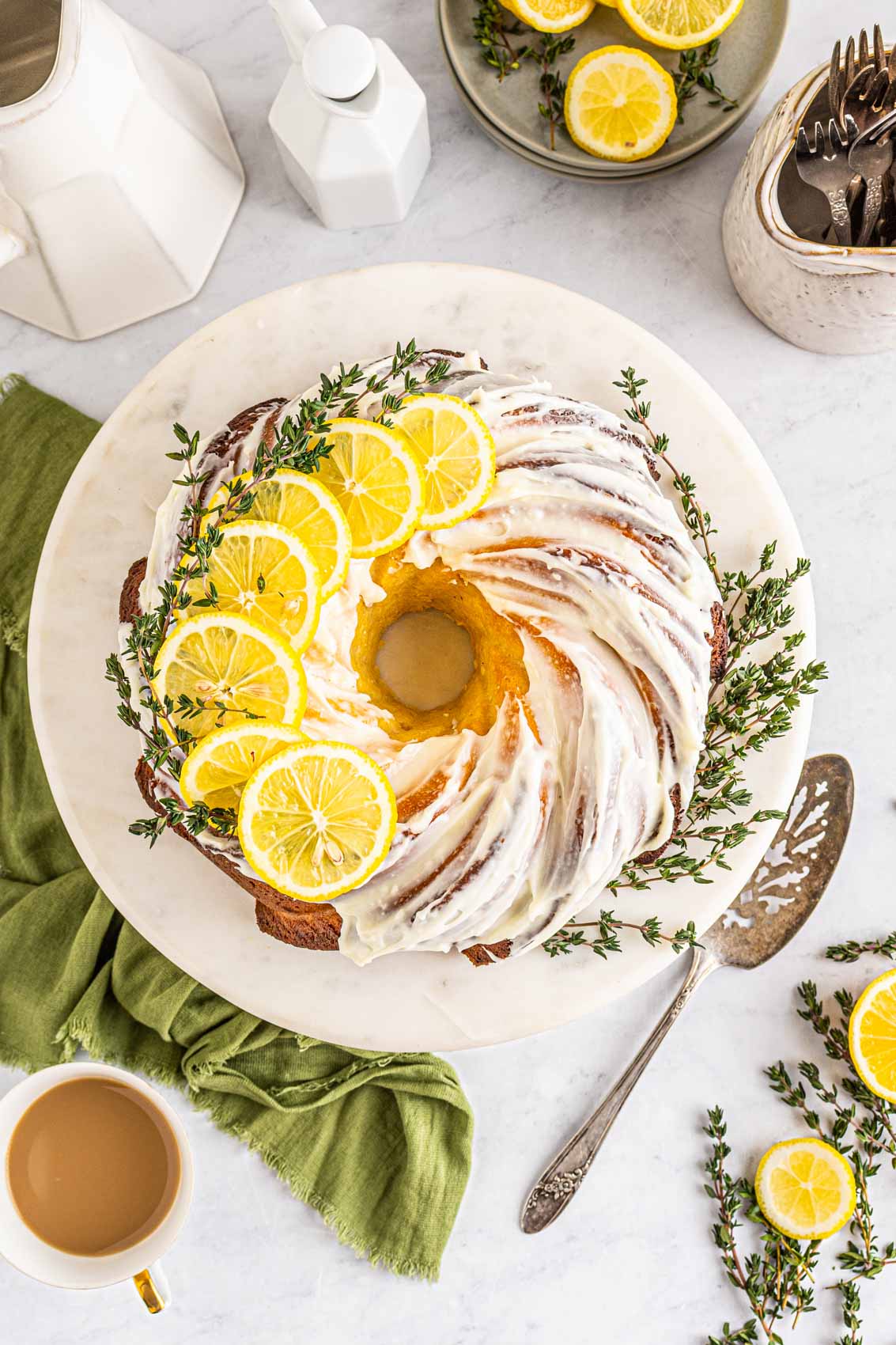 lemon bundt cake with frosting and fresh lemon slices with a coffee mug and seasonings