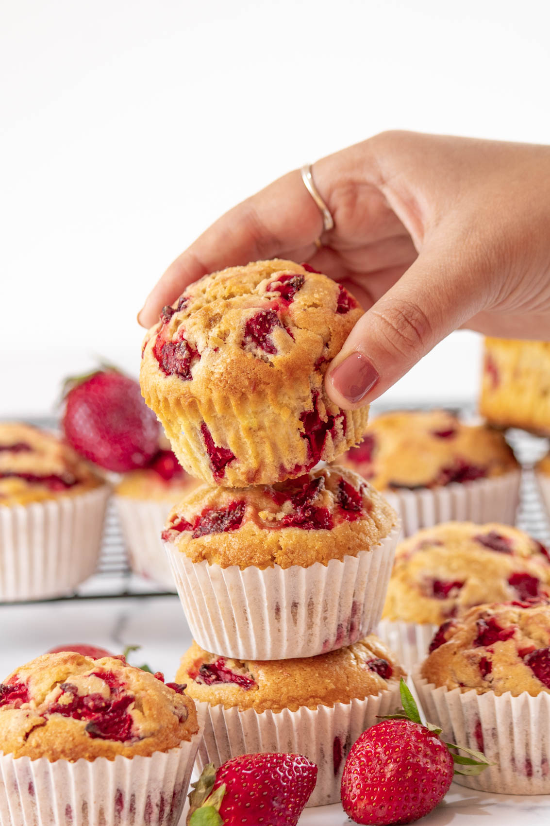 hand grabbing a strawberry muffin from a pile of fresh baked muffins