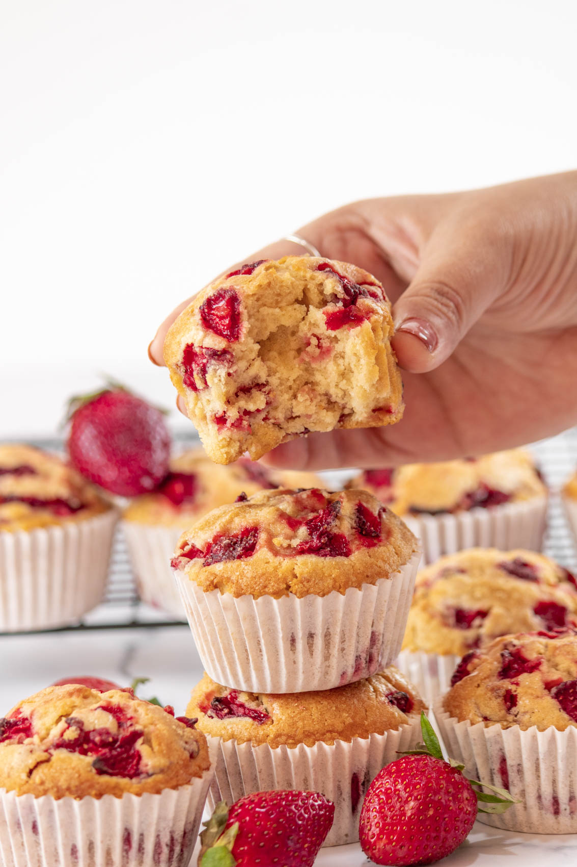 hand grabbing a strawberry muffin with a bite taken from it from a pile of muffins below