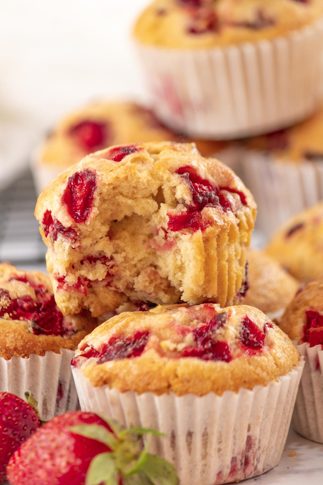 strawberry muffin with a bite taken out piled on top of other muffins