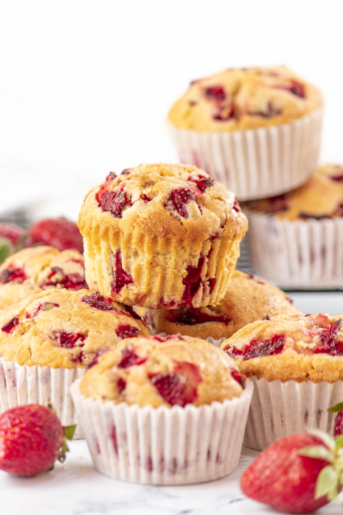 fresh strawberries surrounding golden brown strawberry muffins in a stack