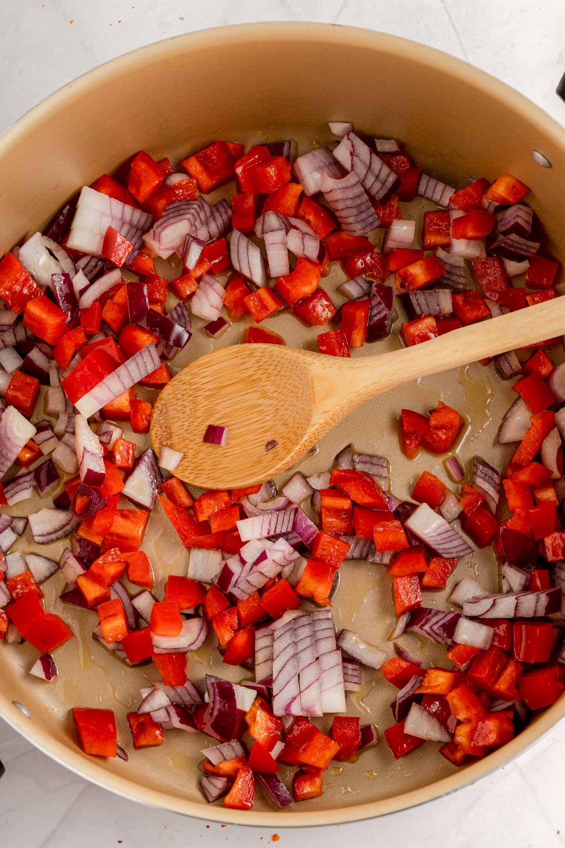 onions and red pepper in a frying pan with a wooden spoon