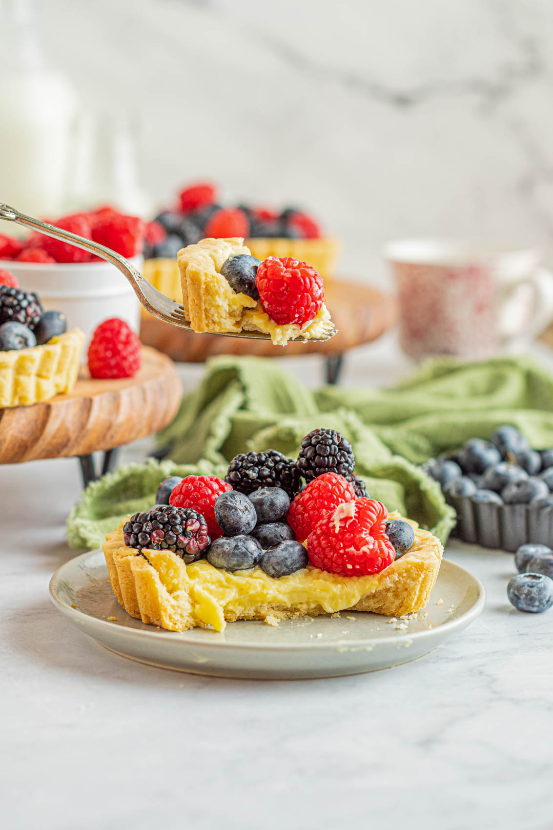 fork holding a bite of custard tartlet with fresh raspberries and blueberries