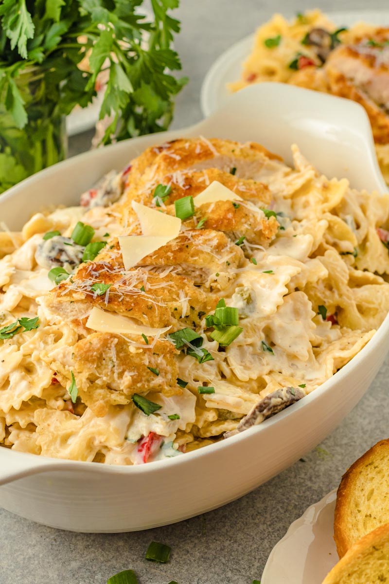 creamy pasta in a casserole dish, topped with parmesan crusted chicken and parmesan shavings