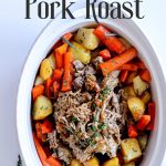pork roast in a large dish surrounded by carrots and potatoes