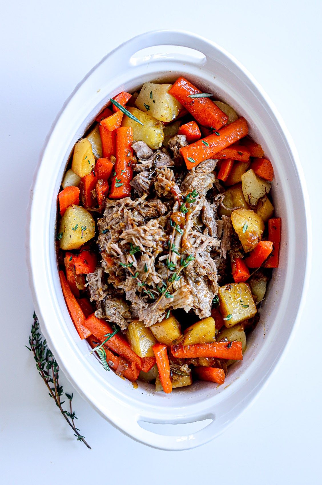 pork roast surrounded by carrots and potatoes in a savory juice with thyme sprinkled about