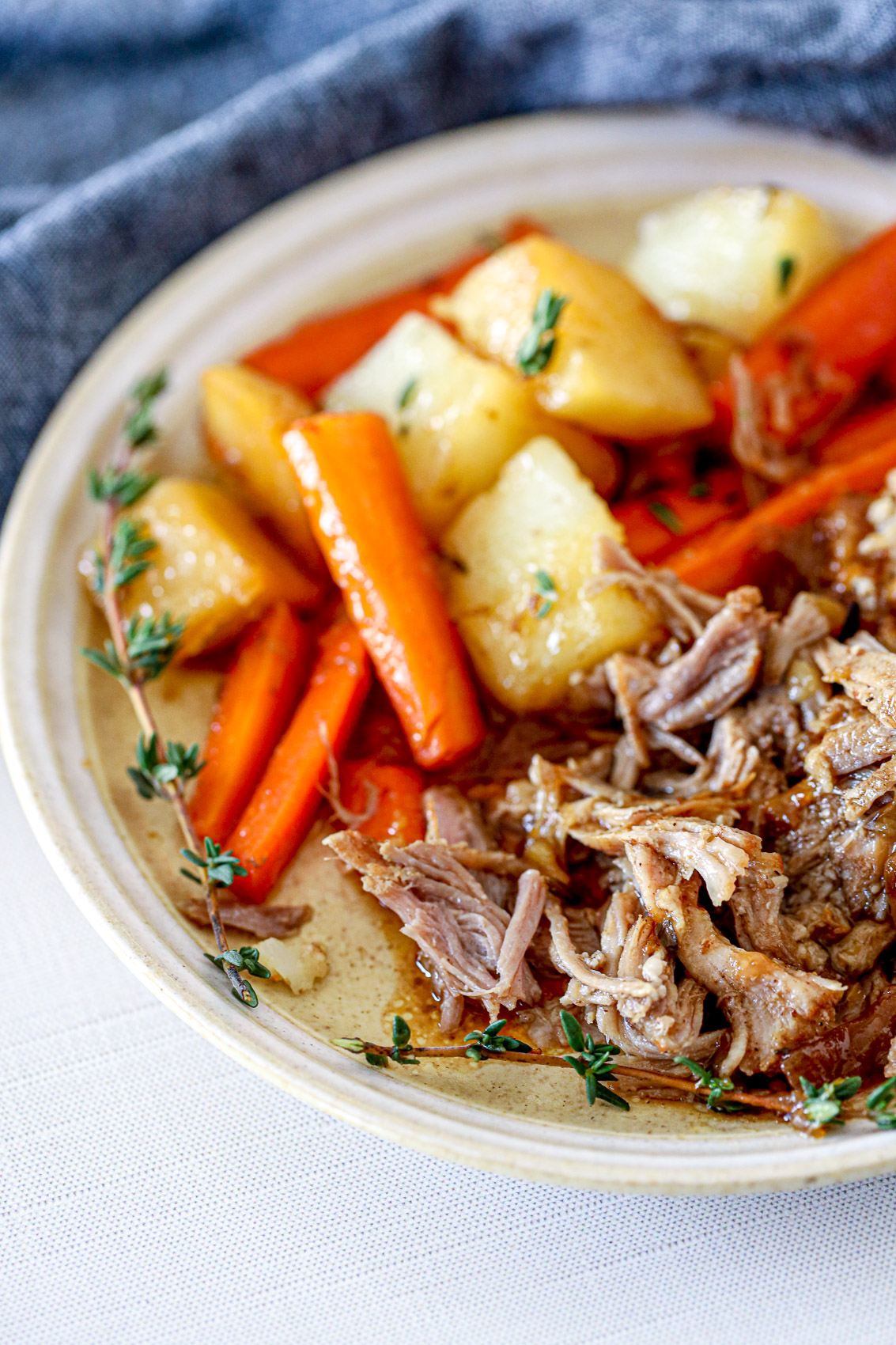 instant pot pork roast with thyme sprigs, potatoes, and carrots in a savory juice