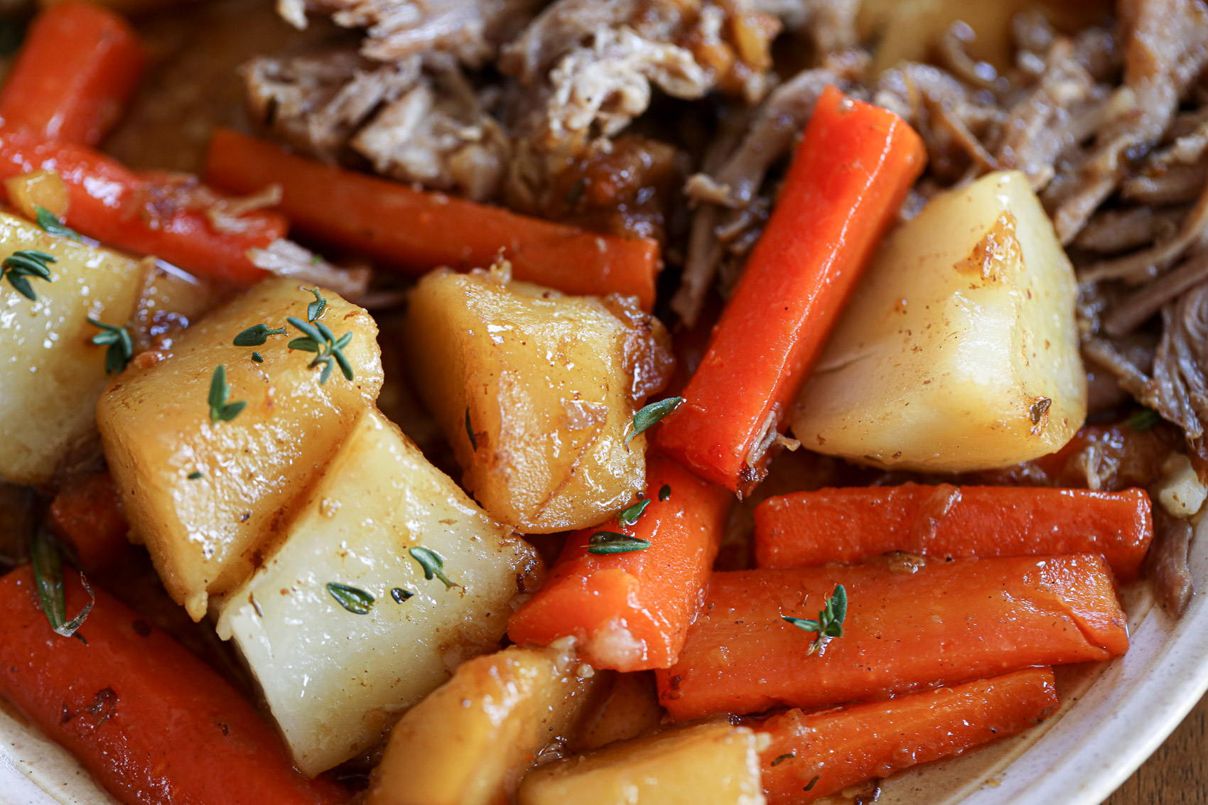 bits of thyme sprinkled on top of a juicy pork roast with carrots and potatoes