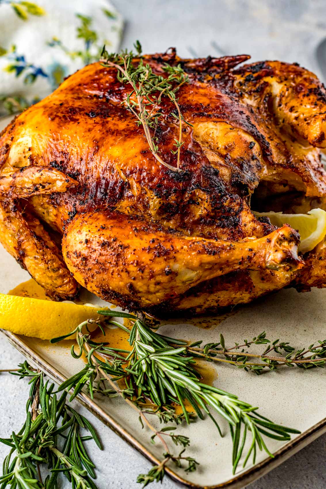 rotisserie style chicken on a platter with lemon wedges, rosemary and thyme seasoning blend