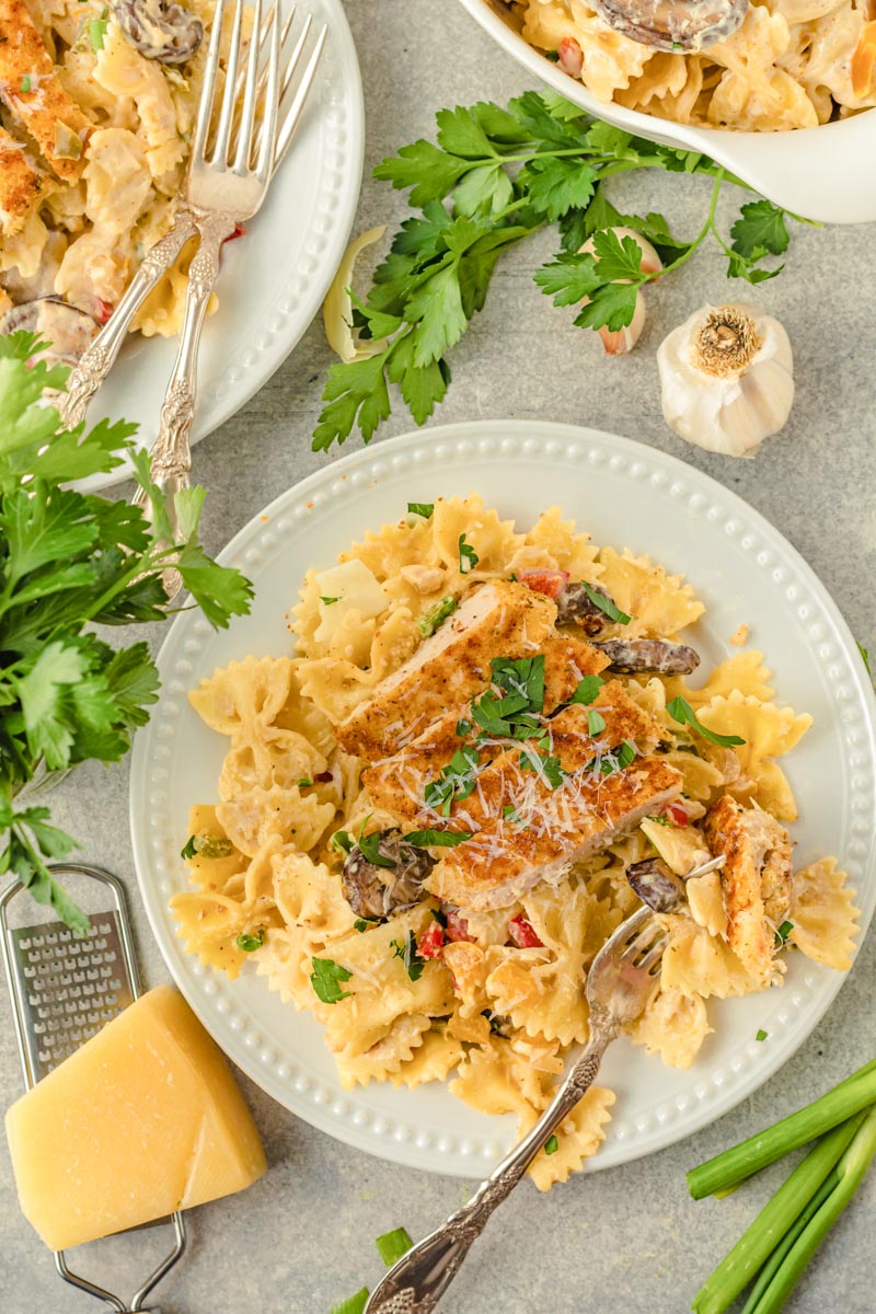 pasta and chicken on a plate next to parsley, green onion, and a block of parmesan cheese and a cheese grater