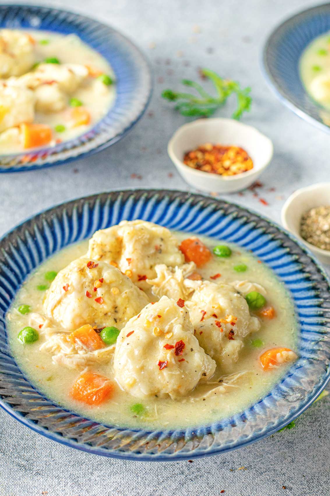 side view of a bowl of chicken and dumplings with peas, carrots, and a thick creamy broth
