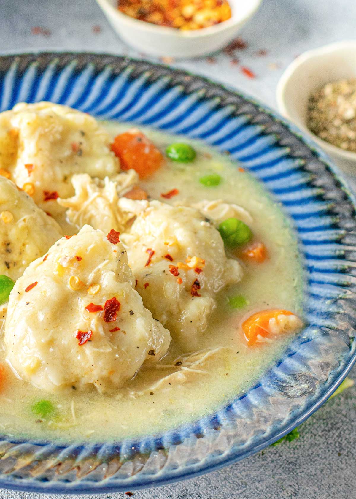close up view of chicken and dumplings in a bowl with peas and carrots
